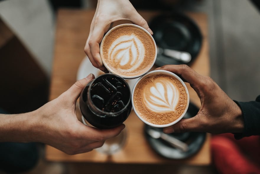 Three hands clinking coffee beverages