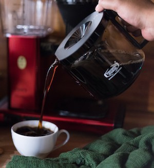 A hand pours coffee from a glass carafe into a small cup
