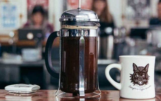 French press on a table next to a mug
