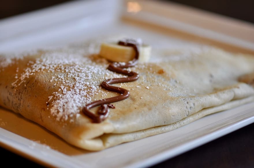 Crepe folded over on a white plate with Nutella drizzled on top