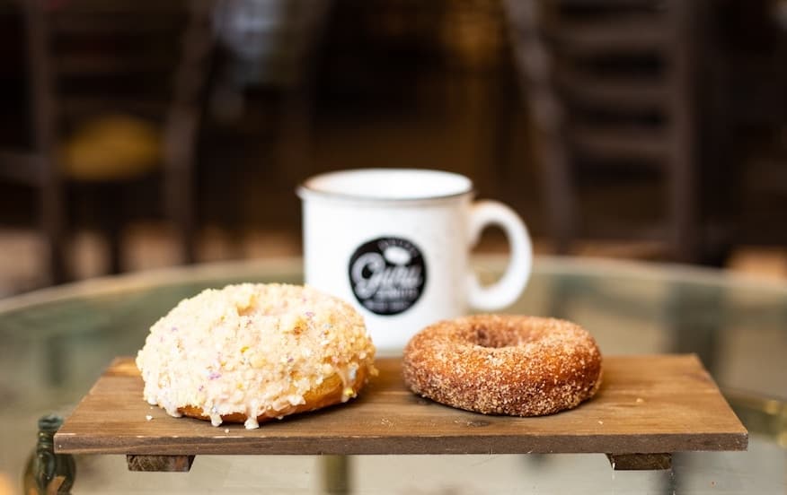 two donuts on a board in front of a cup of coffee