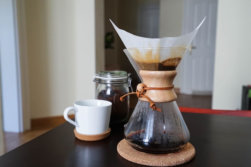 Chemex coffee brewer sitting on a table with a white coffee mug