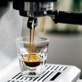 Espresso pouring from a portafilter into a glass cup