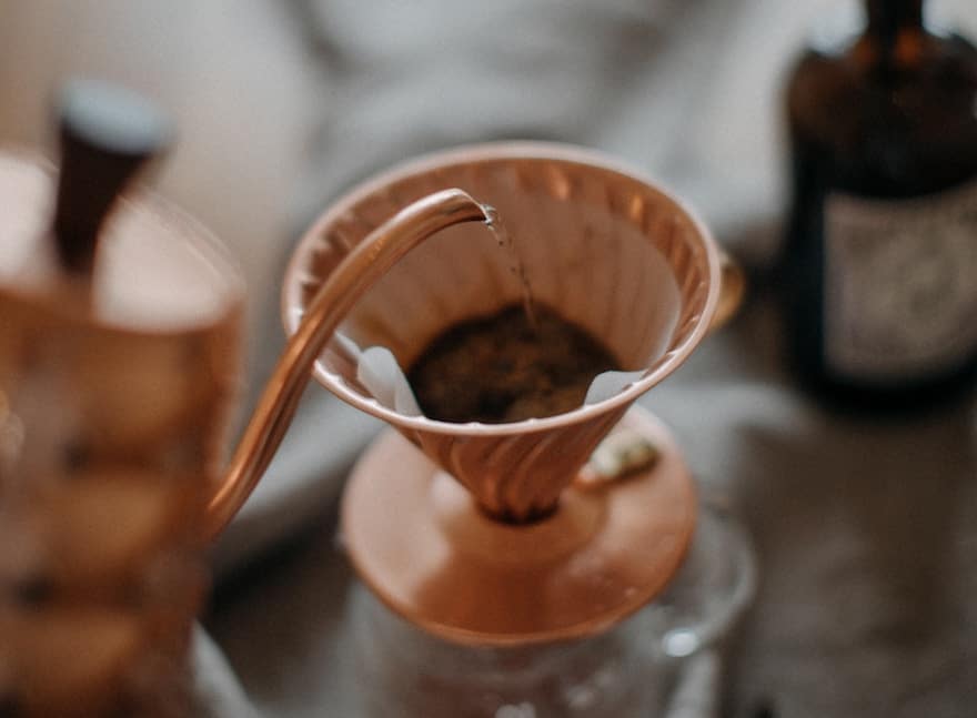 A copper Hario gooseneck kettle pouring into a copper Hario V60 brewer