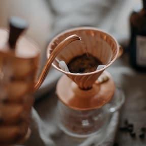 Copper kettle pouring into a copper Hario V60 coffee drip cone