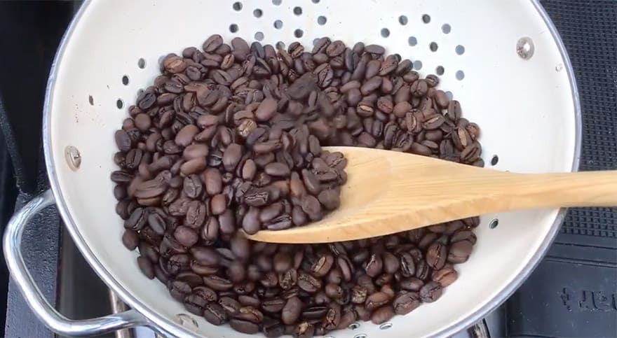 Stirring freshly roasted coffee beans in a colander with a wooden spoon