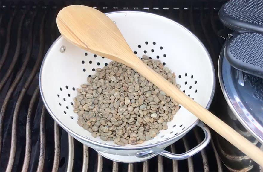 Raw green coffee beans in a colander on the barbecue grill