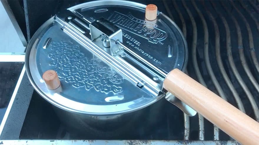 Whirley Pop popcorn popper nestled between the grates of a barbecue grill