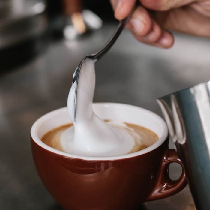A barista tops a standard cappuccino with milk foam.