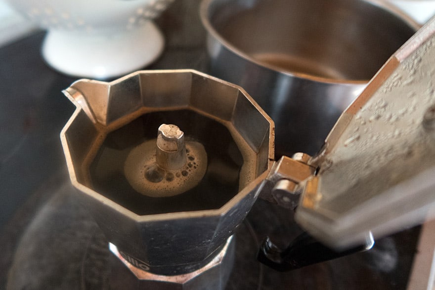 A moka pot fills with coffee on the stove