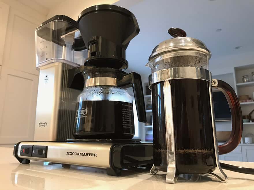 A French press full of coffee next to a drip coffee maker with a full carafe