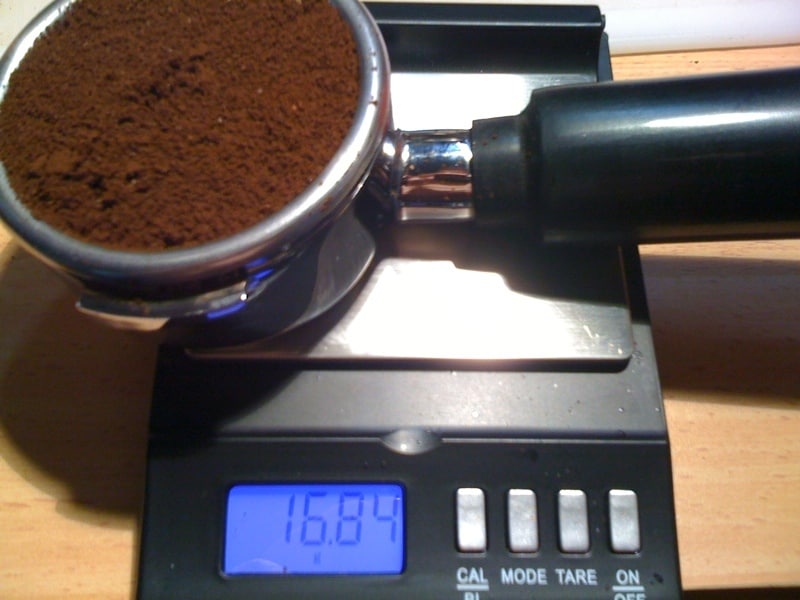A portafilter containing coffee grounds on top of a kitchen scale