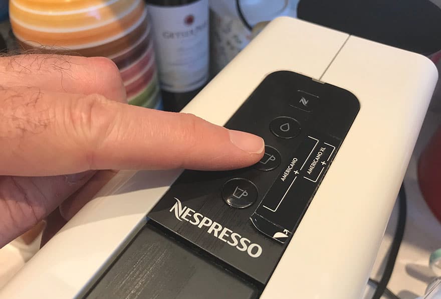 Finger on the lungo button of a Nespresso Essenza Mini