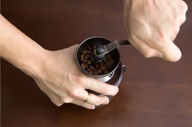 Hands grinding a manual burr coffee grinder