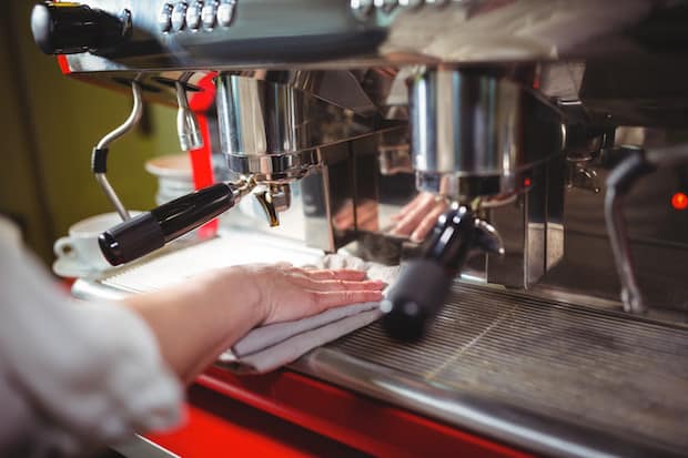 A barista wiping down the drip tray of a commercial espresso machine