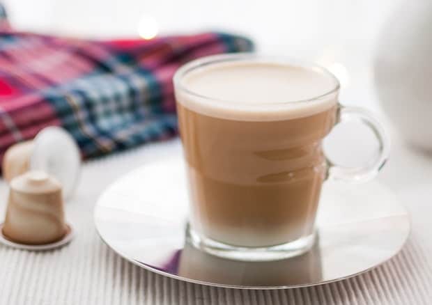 A latte on a table next to some Nespresso capsules