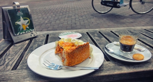 coffee and pastry on a table with a bike passing by in the background