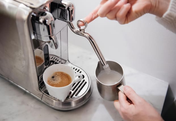 A pair of hands frothing milk with a Nespresso Creatista Plus