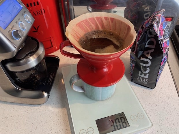 Pour over coffee brewing on a scale next to a bag of coffee from Ecuador