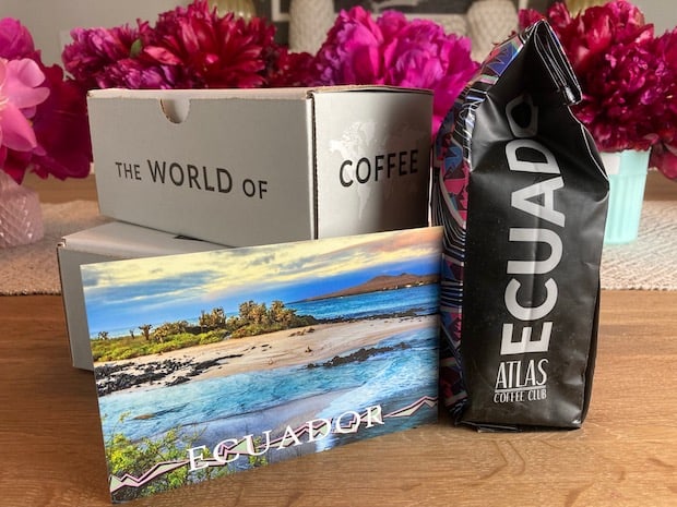 Bag of coffee from Ecuador on a table with a postcard and some flowers