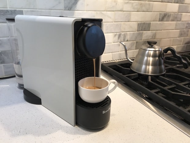 Nespresso Essenza Plus brewing next to a gas stove