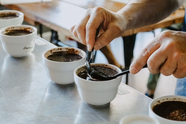 A pair of hands prepares coffee for cupping