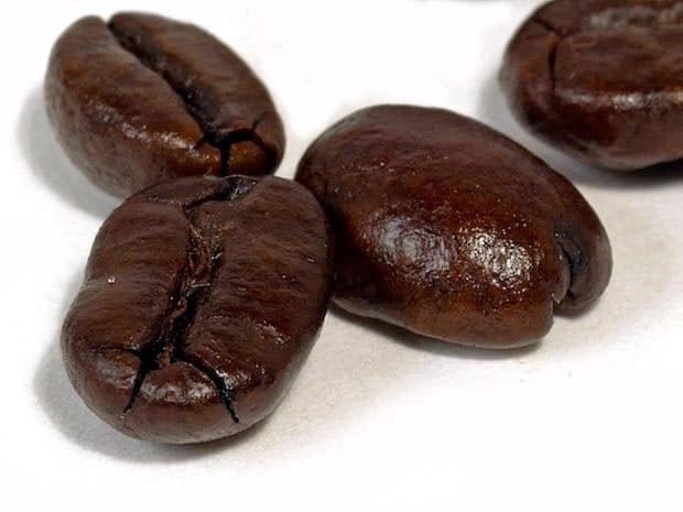 Four dark roasted coffee beans on a white surface