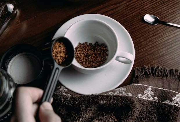 A hand adding instant coffee crystals to a cup using a scoop