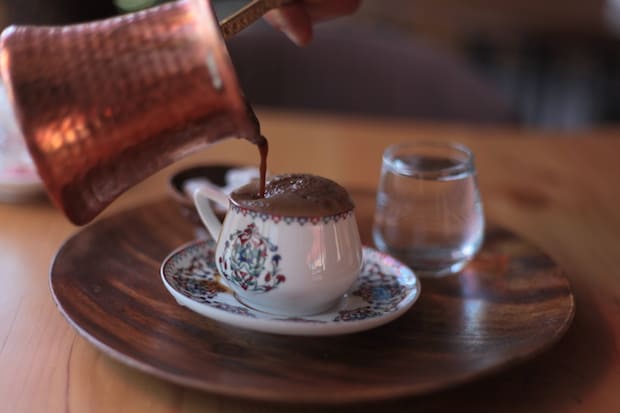 Turkish coffee being poured into a cup from a copper cezve