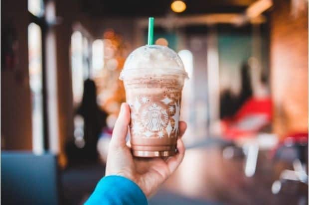 Hand holding up a chocolatey whipped coffee drink inside a Starbucks coffee shop