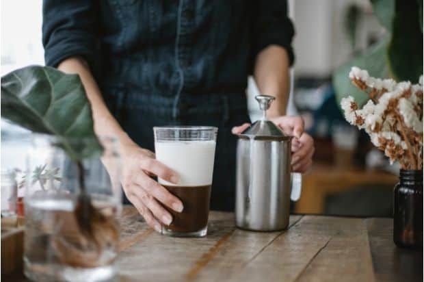 A coffee drink topped with two inches of cold foam in a glass next to a manual milk frother