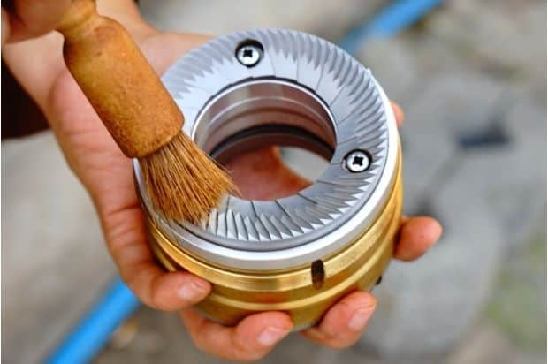 Hands cleaning a stainless steel flat burr from a coffee grinder using a brush