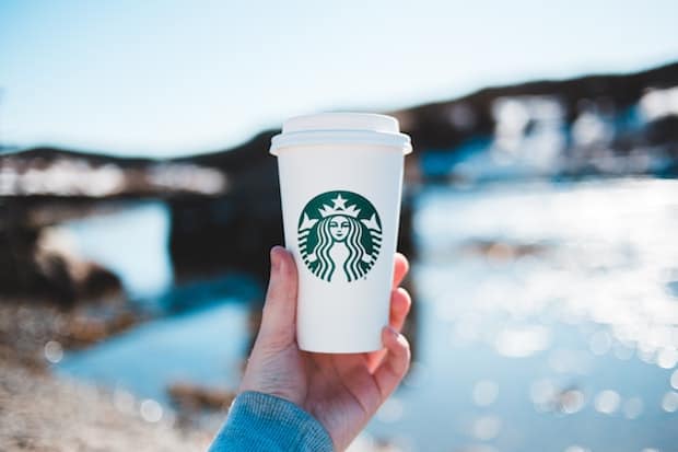 Hand holding up a Grande Starbucks cup with water and a bridge in the background