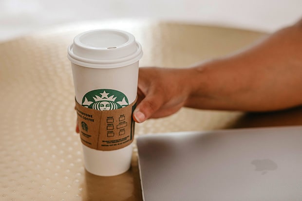 Hand places a Venti Starbucks cup next to a computer