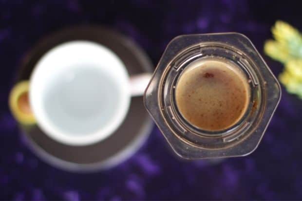Overhead view of an AeroPress coffee maker filled with coffee, next to a cup
