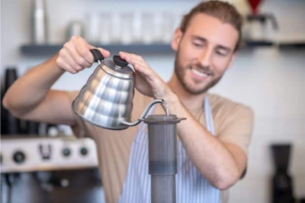 Smiling barista pours from a gooseneck kettle into an AeroPress