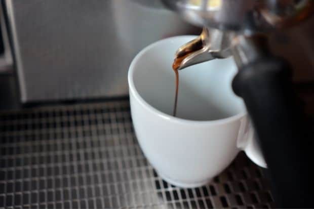 Long shot of espresso pouring from the spout of a machine