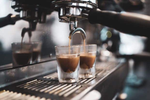 Espresso pouring out of machine into two shot glasses