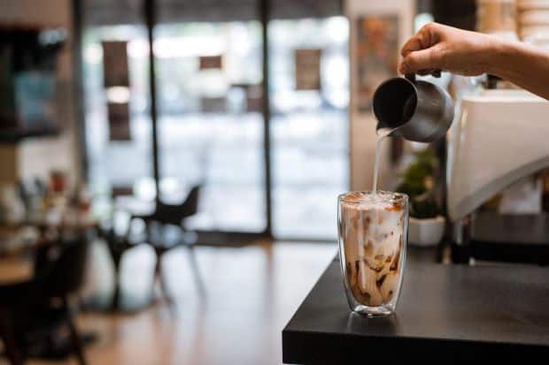Barista pours milk into a large glass of iced coffee