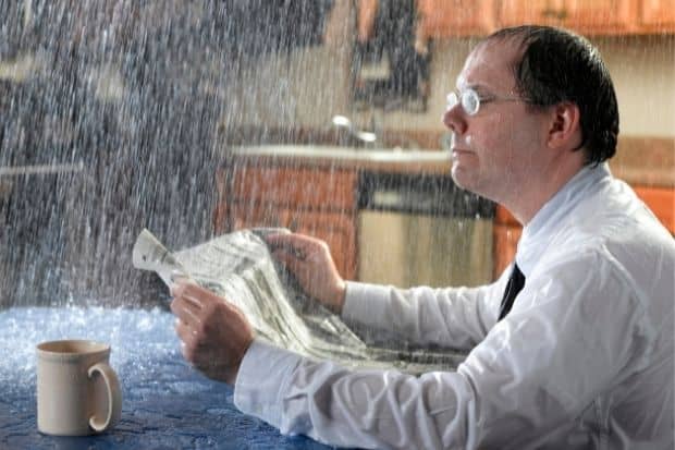Man at kitchen table with coffee getting soaked by rain while reading the paper