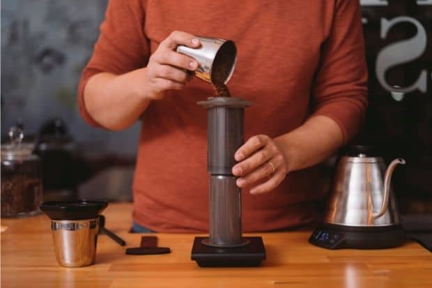 Man pouring coffee grounds into AeroPress coffee maker for comparison between AeroPress metal filter vs. paper