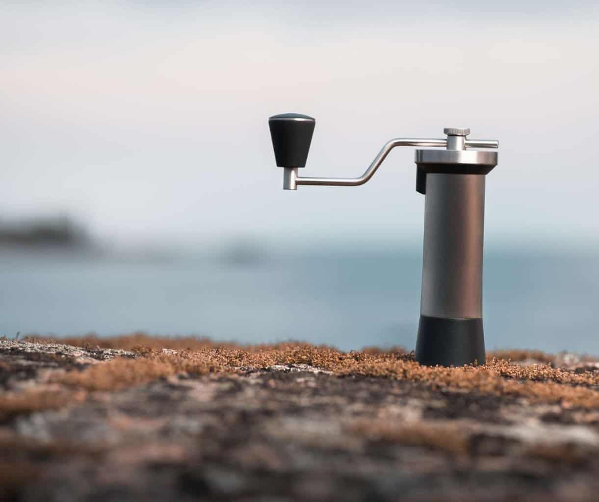 Manual travel coffee grinder standing on a rocky shore by the ocean