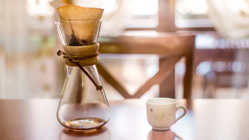 Chemex coffee maker next to a white cup