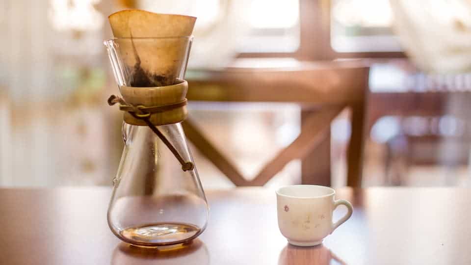 Chemex coffee maker next to a white cup