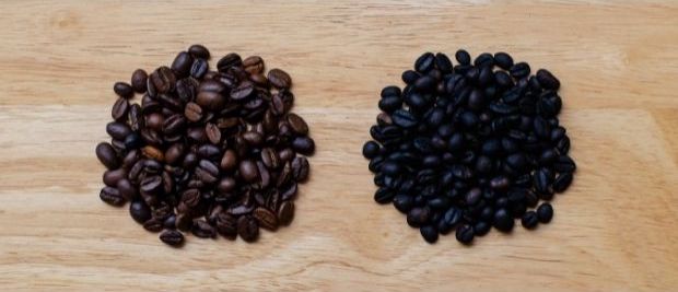 Two small piles of coffee beans on a wooden surface, with a medium roast on the left and a dark roast on the right