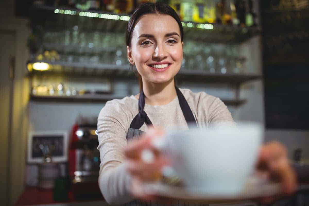 Smiling barista hands a customer her coffee