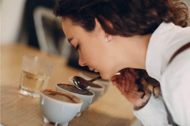 Woman uses a spoon to lift coffee from a cup while tasting