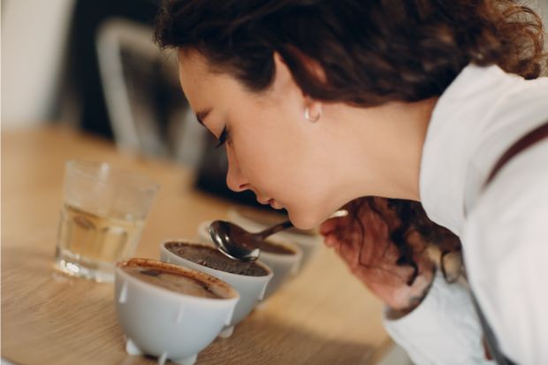Woman smelling coffee with a spoon during a cupping session