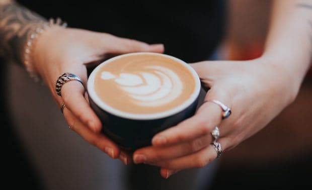 hands holding a latte with decorative milk foam on the surface