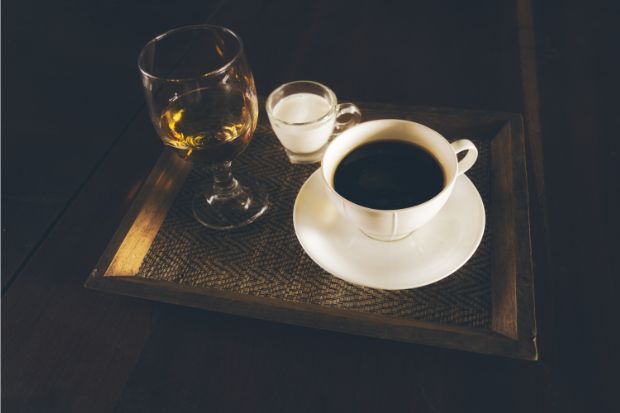 Cup of coffee next to glass of whiskey that can work as a liquor for coffee